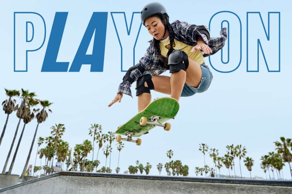 A young asian woman skateboarding with the words Play On floating behind her.